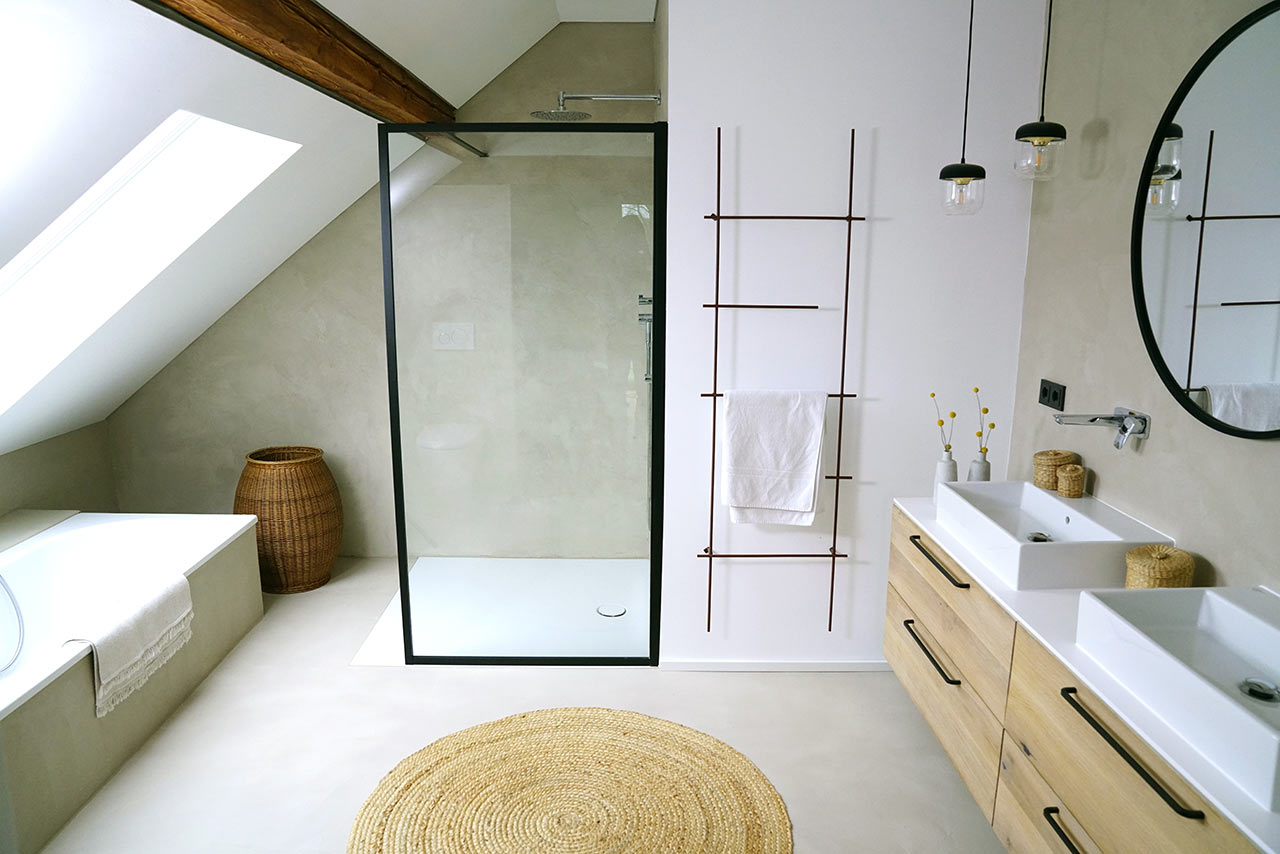 Moderní minimalistická koupelna v patře domu s čistým designem a střešním oknem pod bytelným trámem z masivu