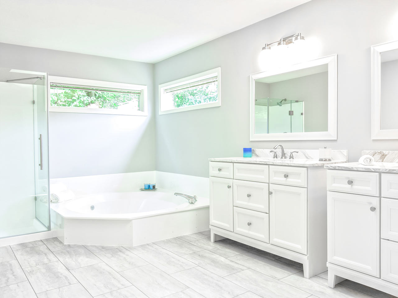Prostorná a světlá bílá koupelna s rohovou vanou a vyvýšeným sprchovým koutem s prosklenými dveřmi