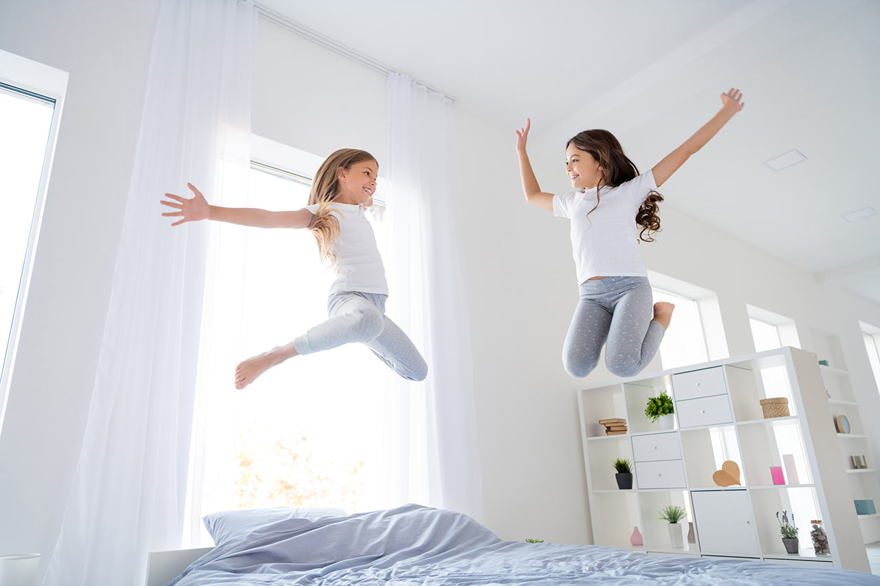 Šťastné děti skáčou na nízké posteli v ložnici s vysokými stropy