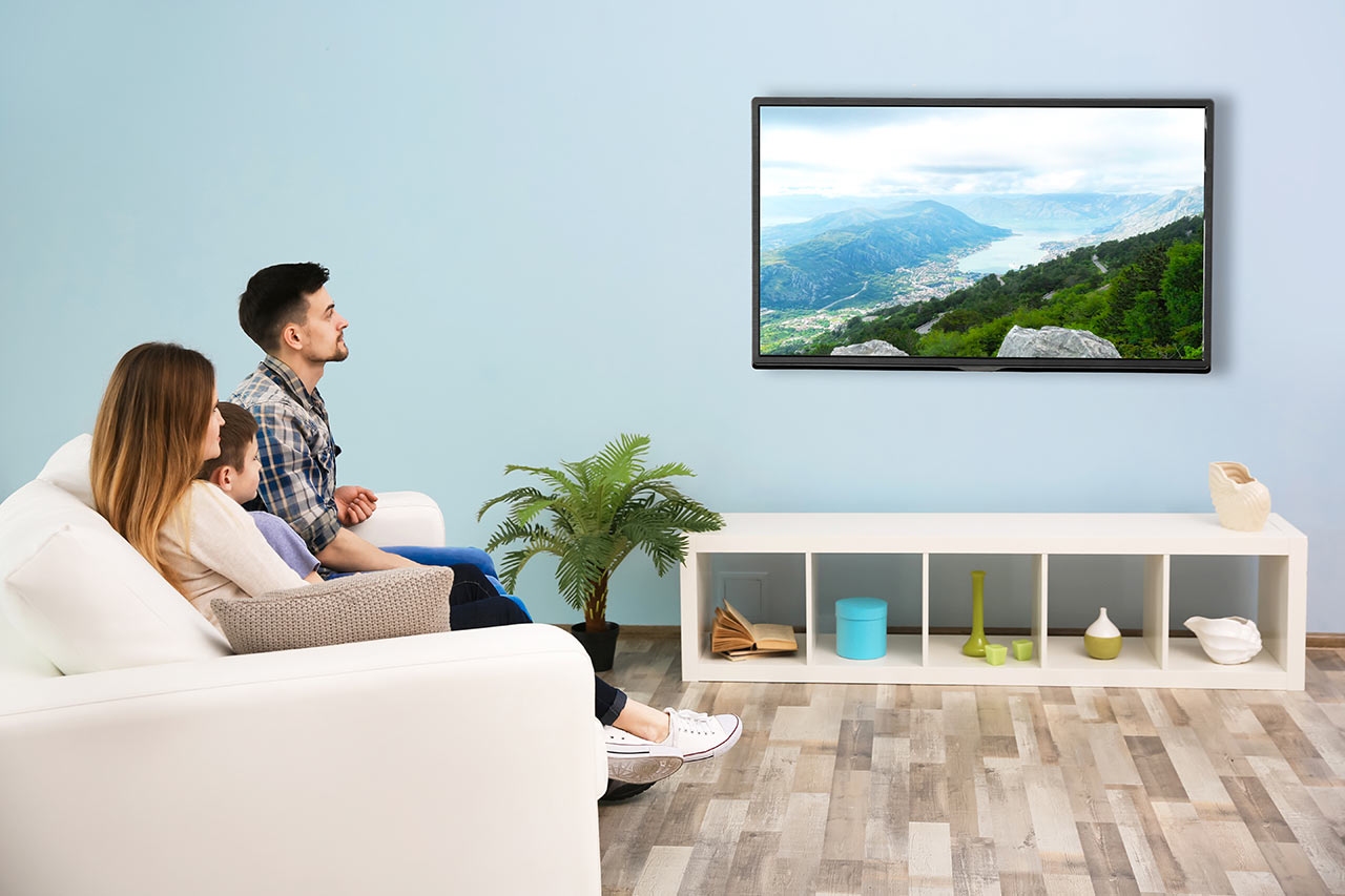 Designová televize s krajinou na obrazovce, kterou sleduje rodina na sedačce