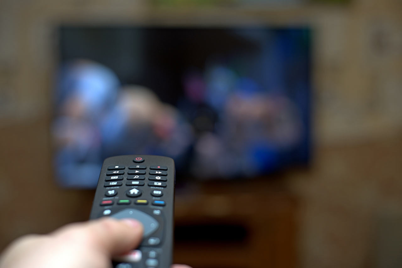 Televize a ruka s ovladačem v rozmazaném obývacím pokoji